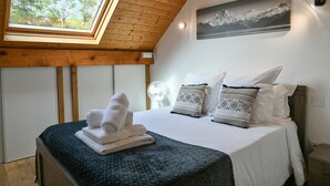 Ein Schlafzimmer mit Oberlichter, einem Bett mit weißer Bettwäsche, gemusterten Kissen und einem Berglandschaftsbild an der Wand.