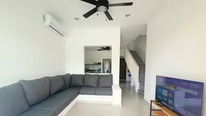 Una sala de estar moderna con un sofá seccional gris, un televisor de pantalla plana sobre un mueble de madera y un ventilador de techo.