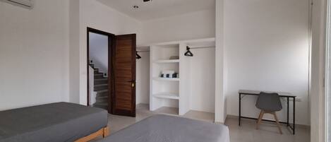 A room with two single beds, a desk, a chair, a wardrobe, a ceiling fan, and a staircase.