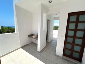 Un balcon avec vue sur l’océan, un petit lavabo et une porte dont les panneaux sont en verre dépoli.