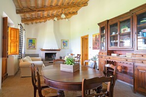 A dining area with a wooden table, chairs, a fireplace, and a cabinet with glass doors. - ORZALUME FARMHOUSE (Umbria)