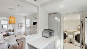 A modern kitchen with a built-in oven, a dining area with a white table and chairs, and a laundry area with a washing machine and dryer. - The Rutledge Roost of Charleston (Charleston)