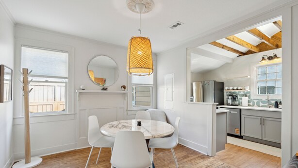 A modern kitchen with white cabinets, a stainless steel refrigerator, and a dining area with a round table and white chairs. - The Rutledge Roost of Charleston (Charleston)