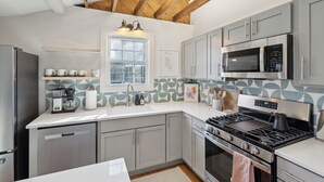 A modern kitchen with grey cabinets, a stainless steel refrigerator, a microwave, and a gas stove. - The Rutledge Roost of Charleston (Charleston)