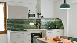 Una cocina moderna con armarios blancos, salpicadero de azulejos verdes, microondas y comedor con mesa y sillas de madera.