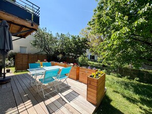 A wooden deck with outdoor furniture, raised garden beds with flowers, and a view of a residential area.