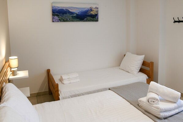 A hotel room with two single beds, a nightstand with a lamp, a painting on the wall, and a wooden headboard.