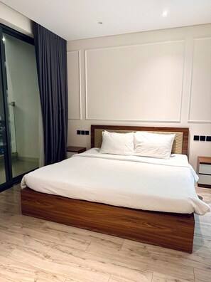 Una habitación de hotel moderna con una cama grande, cabecera de madera y una puerta de cristal que da a un balcón.