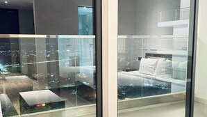 Un dormitorio moderno con un ventanal grande, una cama y una mesita de noche blanca.