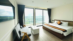 Habitación de hotel moderna con una cama grande, un escritorio y vistas a un paisaje urbano a través de amplias ventanas.