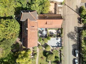 Vue aérienne d’un bâtiment doté d’un toit recouvert de tuiles, d’une zone de stationnement et d’un espace vert environnant.