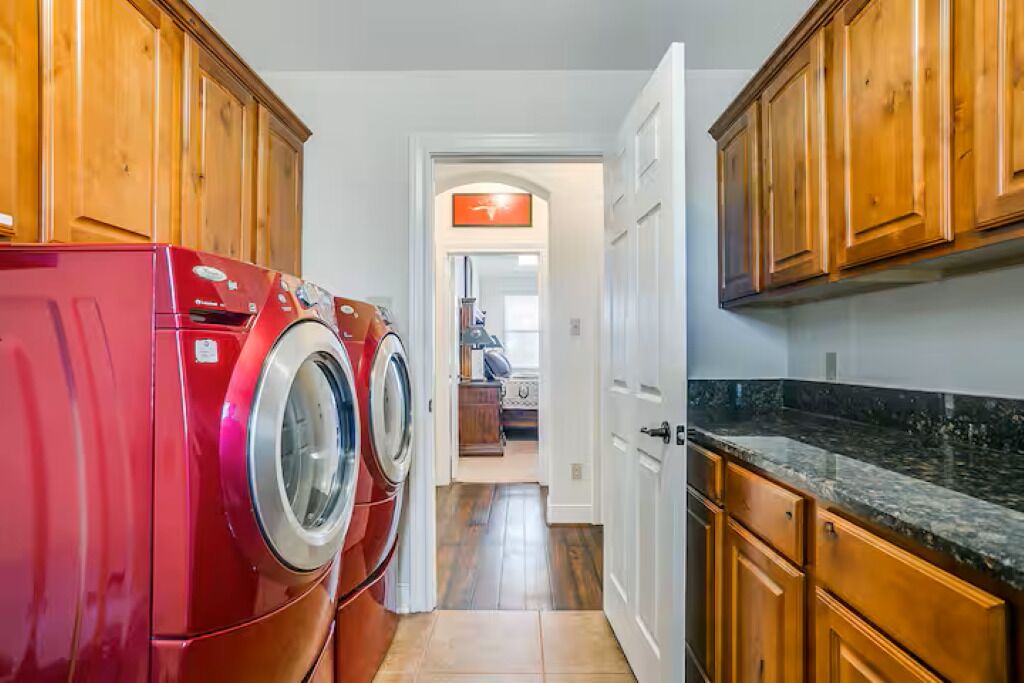 A laundry room with two red front-loading washers and dryers, wooden cabinets, and a kitchen area with granite countertops.