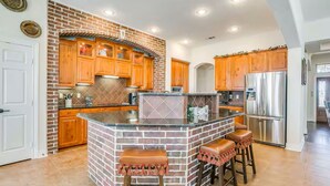A kitchen with a brick island, wooden cabinets, stainless steel appliances, and a white door. - Charming house with AC and fitness room in enjoyable Fort Worth (Fort Worth)