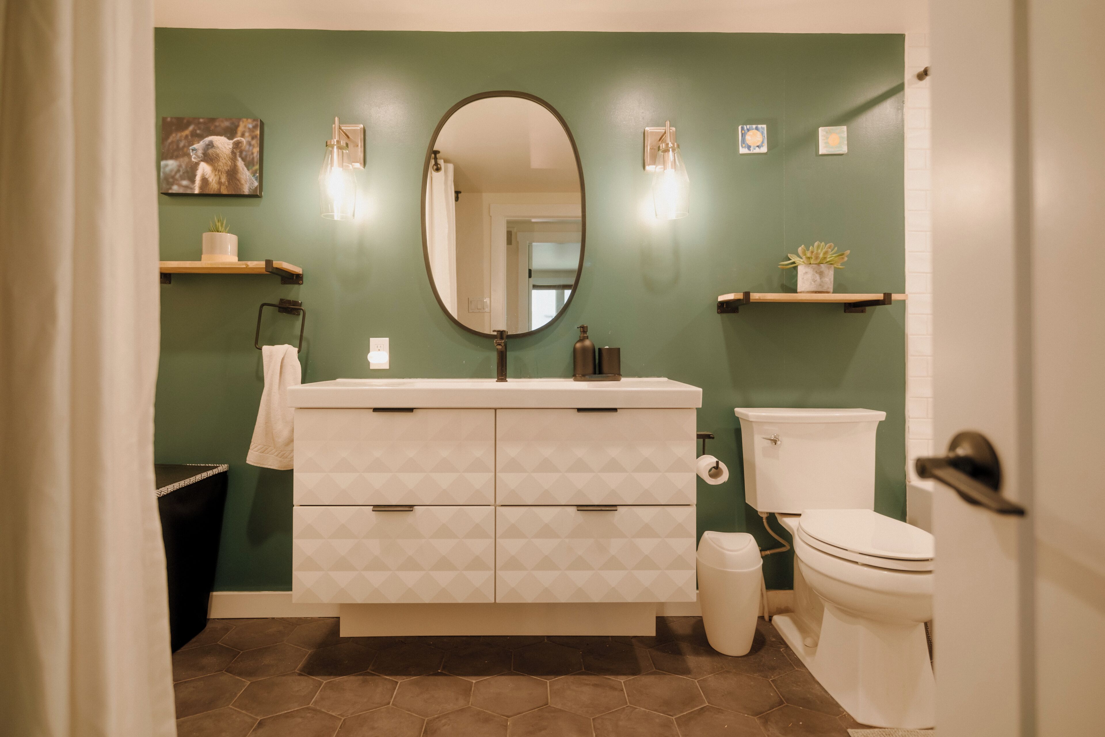 A bathroom with a white vanity, a round mirror, a toilet, and green walls.