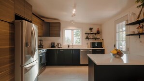 A modern kitchen with stainless steel appliances, dark cabinets, and a central island with a bowl of fruit. - Character 3-bdr Newly Reno'd Modern OceanSky Lodge (Britannia Beach)