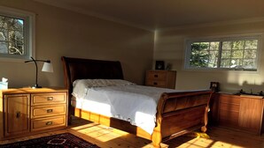 Un dormitorio con una cama de madera, una mesita de noche, un aparador, una ventana y una alfombra estampada.