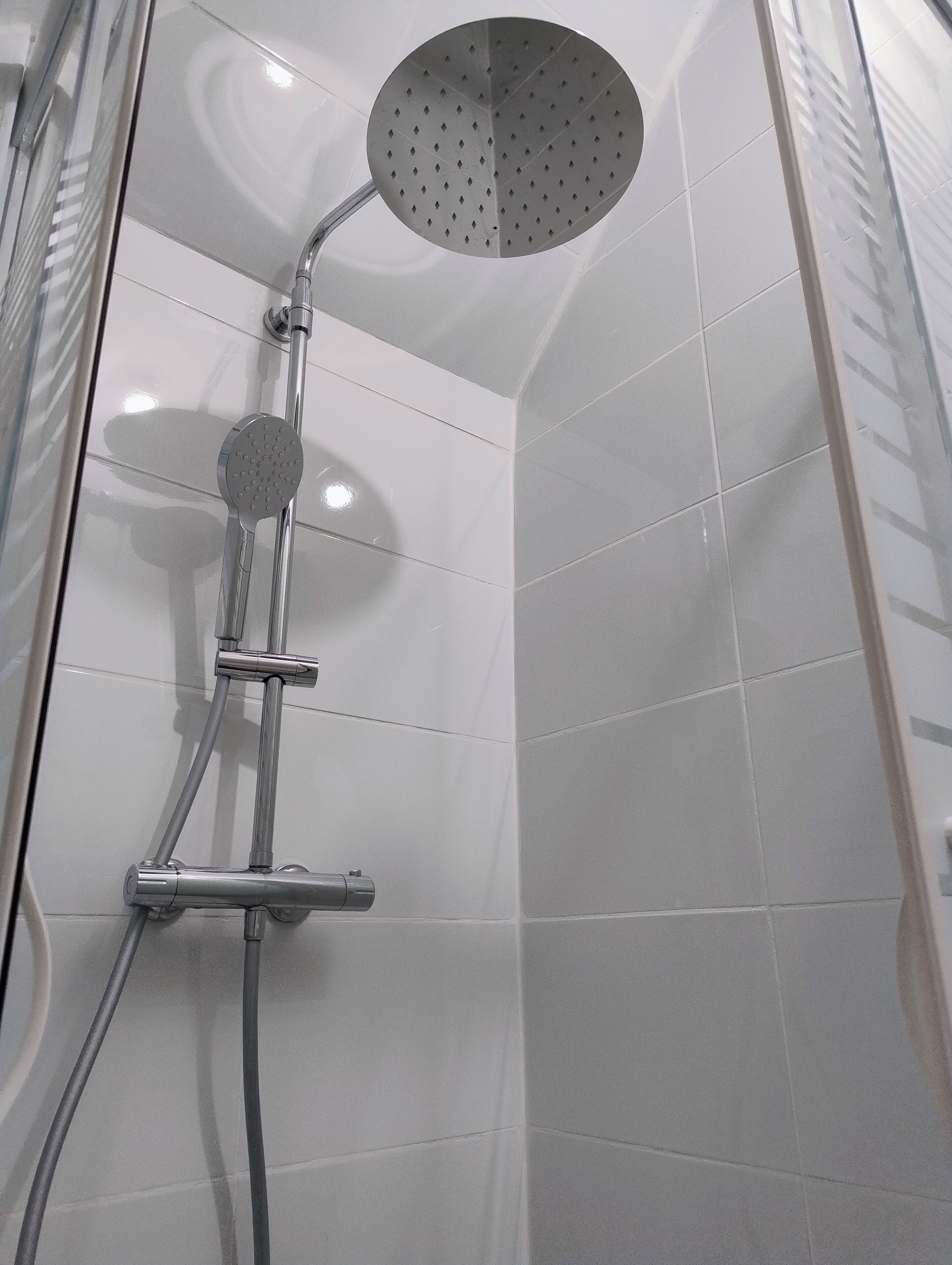 Een douche met een handdouche en een vaste douchekop in een betegelde badkamer.