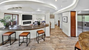 Una cocina moderna con una isla curva, taburetes de bar, un televisor de pantalla plana y piso de baldosas de piedra.