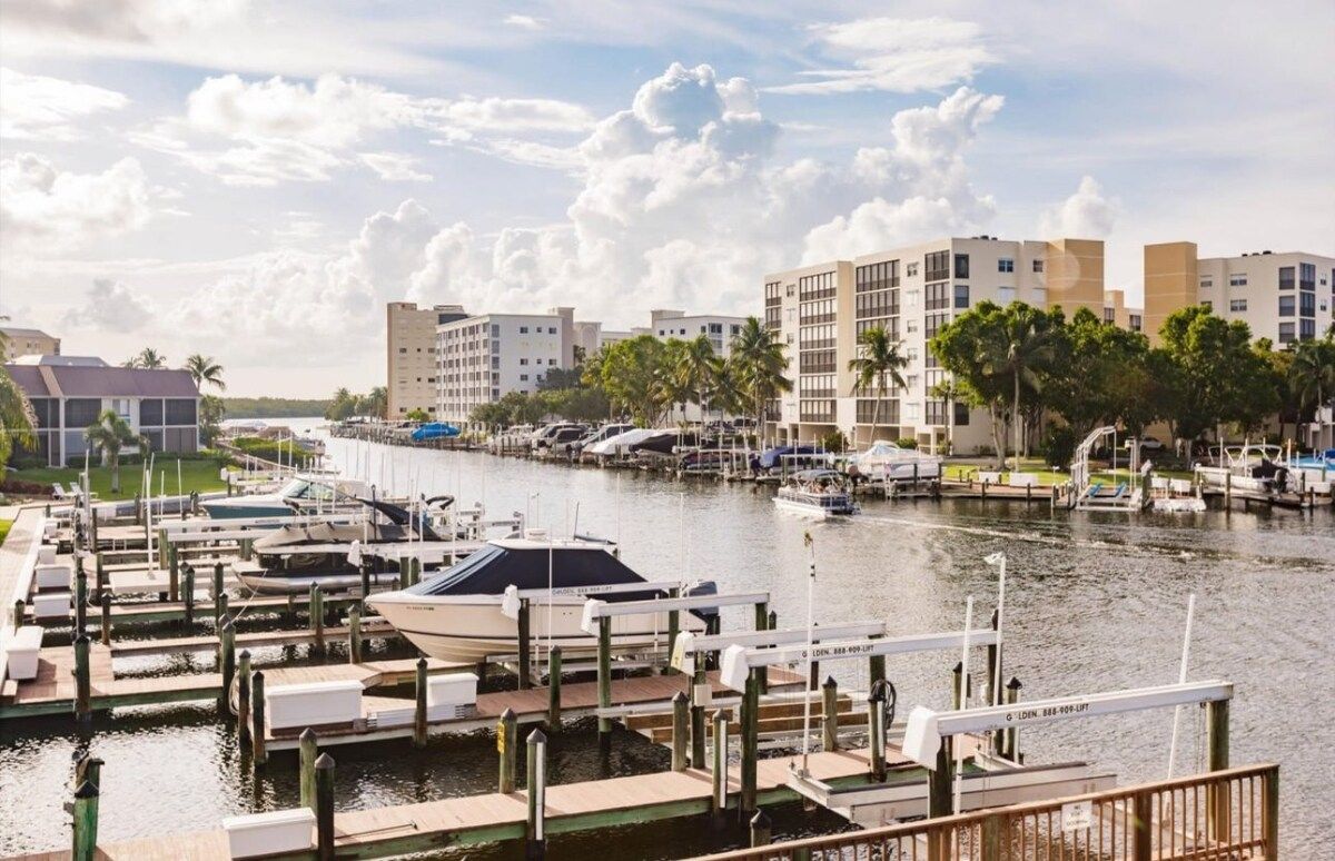 A marina with boats docked, a waterway, and buildings in the background.