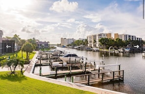 A marina with boats docked, a water canal, and buildings in the background.