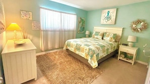 A bedroom with a bed, bedside tables, a lamp, a window with curtains, and wall decorations.
