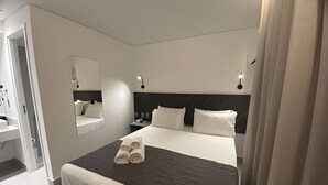 Et moderne hotelværelse med en stor seng, et sengebord, et natbord, et spejl og udsigt til badeværelset.