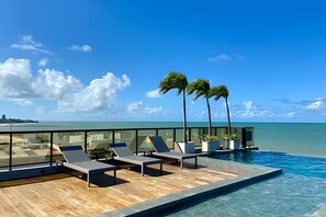 A rooftop infinity pool with lounge chairs and palm trees, overlooking a beach and ocean. - Arpoar (Joao Pessoa)