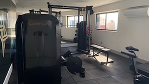 Et fitnessrum med forskellig træningsudstyr, herunder en squat-stativ og vægtbænke.