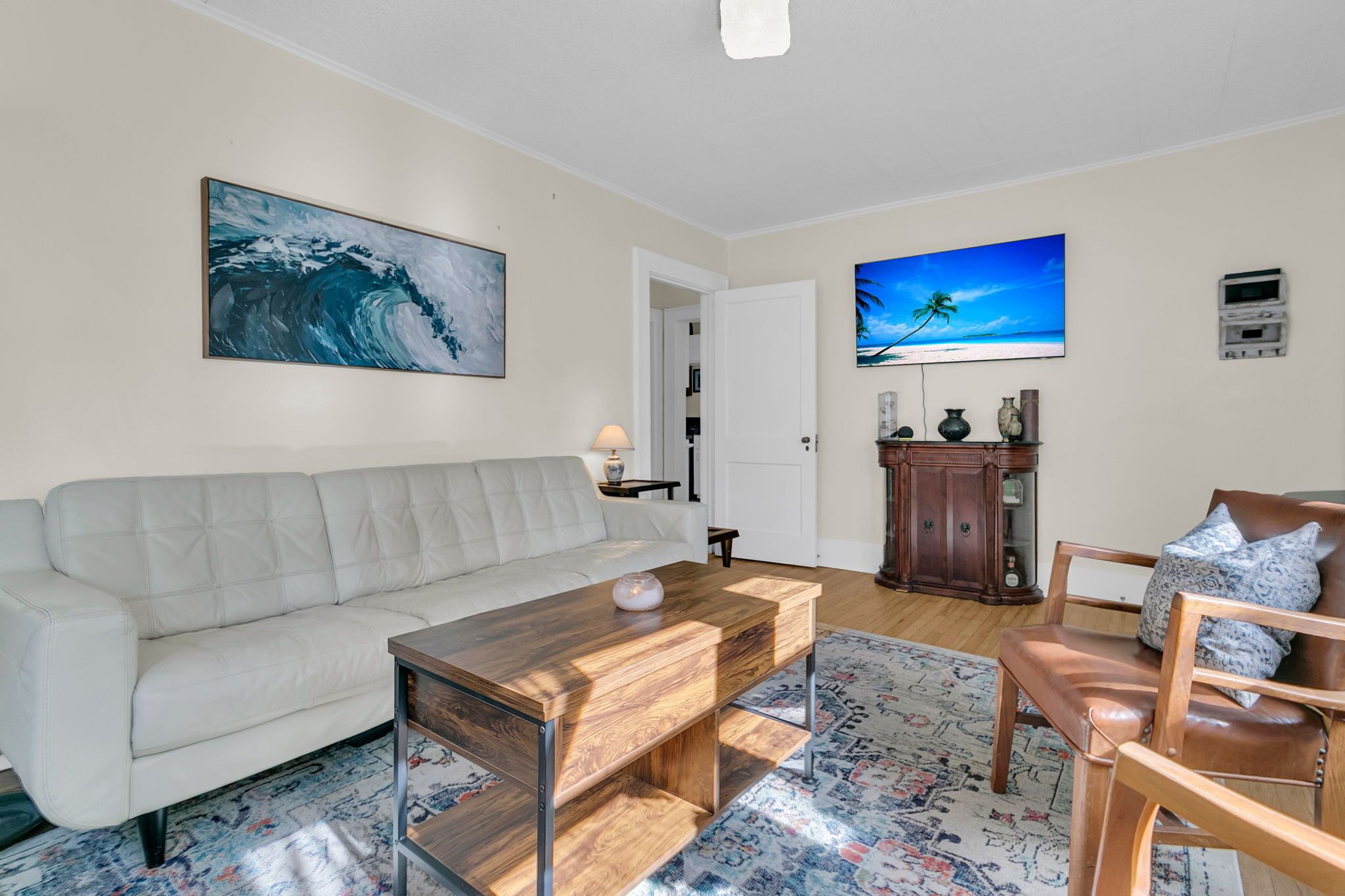 A living room with a white sofa, a wooden coffee table, a patterned rug, and a television on the wall.