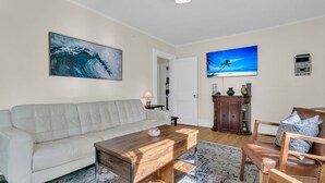 A living room with a white sofa, a wooden coffee table, a patterned rug, and a television on the wall. - Downtown Bungalow with Fenced Yard, Walkable to Restaurants, Dog Friendly (Charleston)