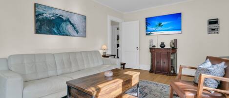 A living room with a white sofa, a wooden coffee table, a patterned rug, and a television on the wall.