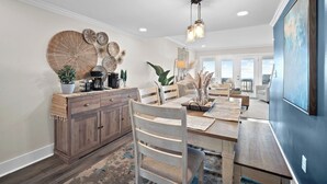 A spacious dining area with a wooden table and chairs, a coffee station, and a large wall art piece. - Oceanfront Villa, Private Pool, Beautiful Beach Views - 410 Captain John Fripp (Fripp Island)