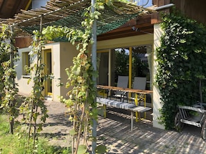 A covered outdoor seating area with a table and chairs, a pergola with climbing plants, and a bicycle parked nearby. - Apartment 'Müllerleile' with Shared Pool, Terrace and Wi-Fi (Gengenbach)