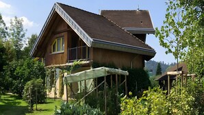Une maison en bois avec un toit en pente, un balcon et un jardin où poussent différentes espèces de plantes.