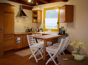 A kitchen with wooden cabinets, a window with blinds, a coffee maker, and a dining area with white chairs. - Apartment 'Müllerleile' with Shared Pool, Terrace and Wi-Fi (Gengenbach)
