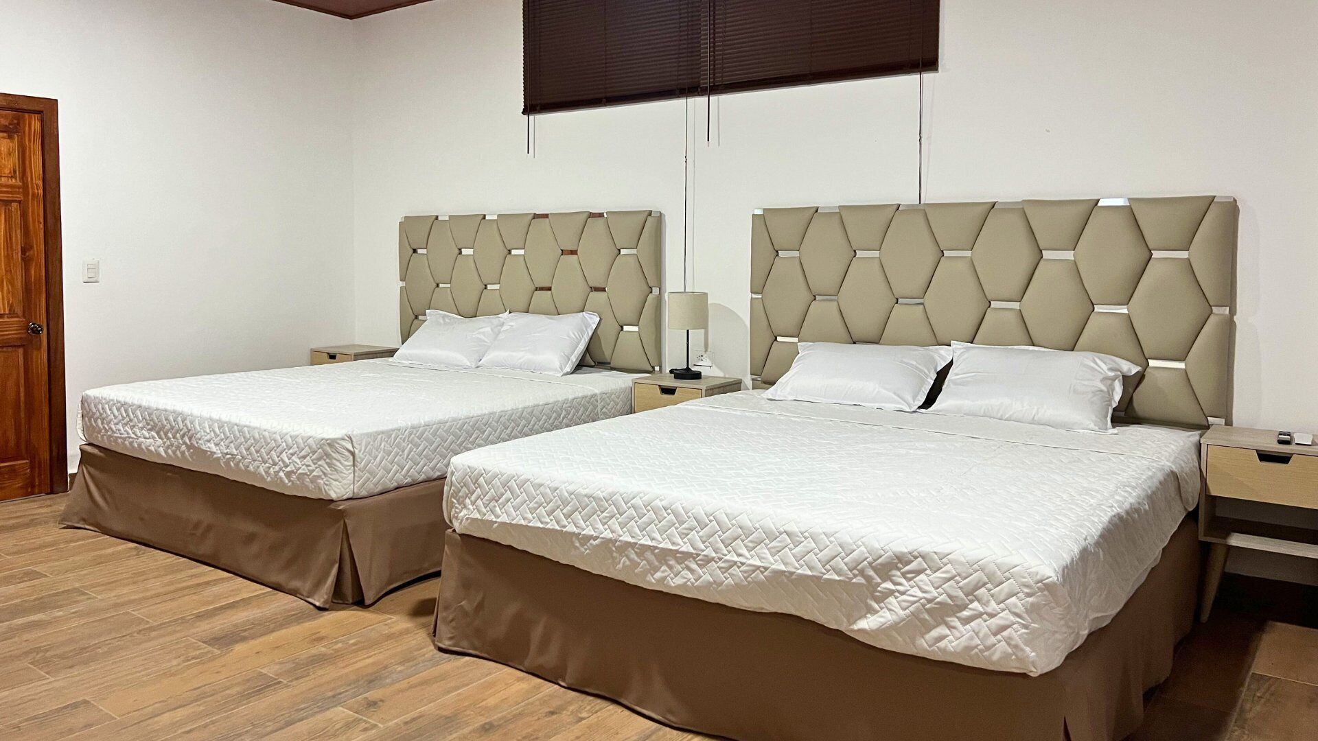 Camera d'albergo con due letti, ognuno dotato di poggiatesta, comodini e lampada.