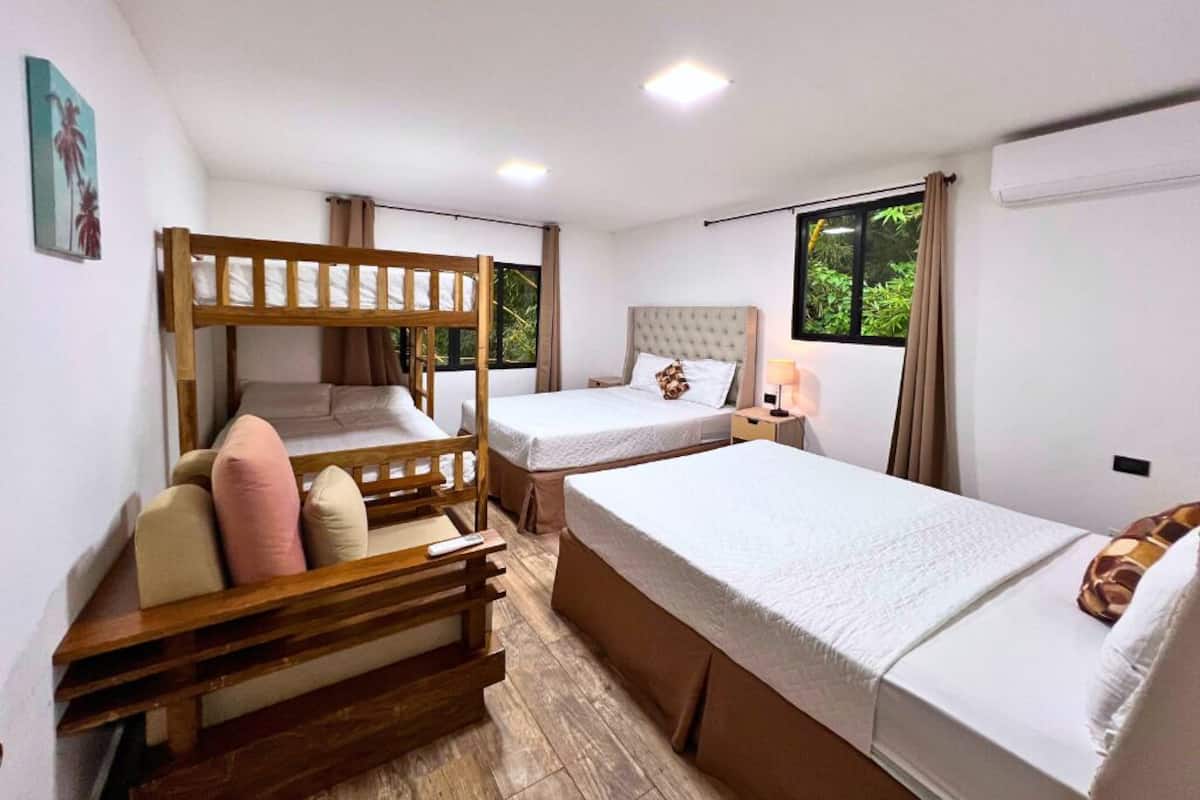 A hotel room with bunk beds, a single bed, and a nightstand with a lamp.
