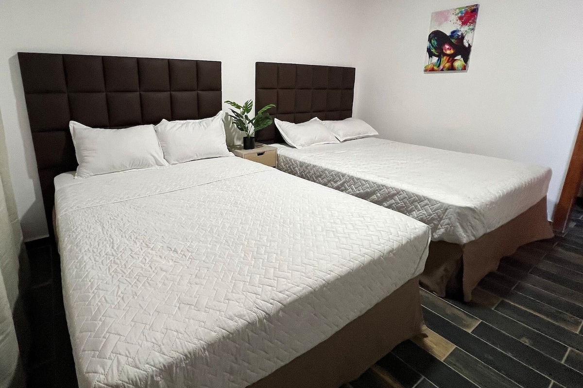 A hotel room with two beds, each with a headboard and white bedding.
