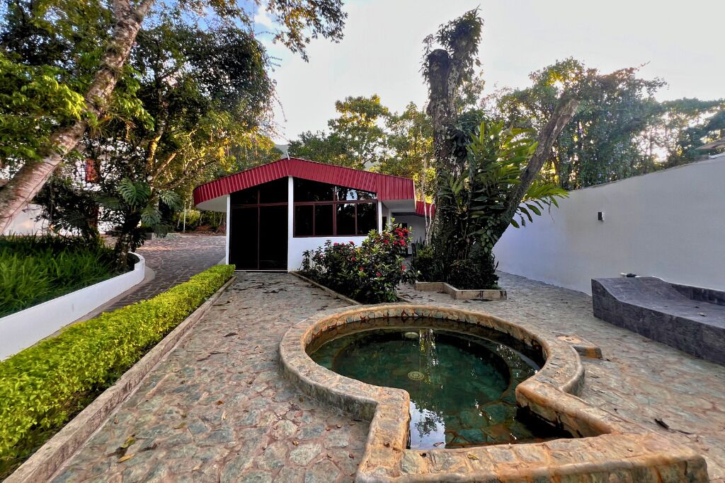 A courtyard with a stone pool, a small building with a red roof, and lush greenery.