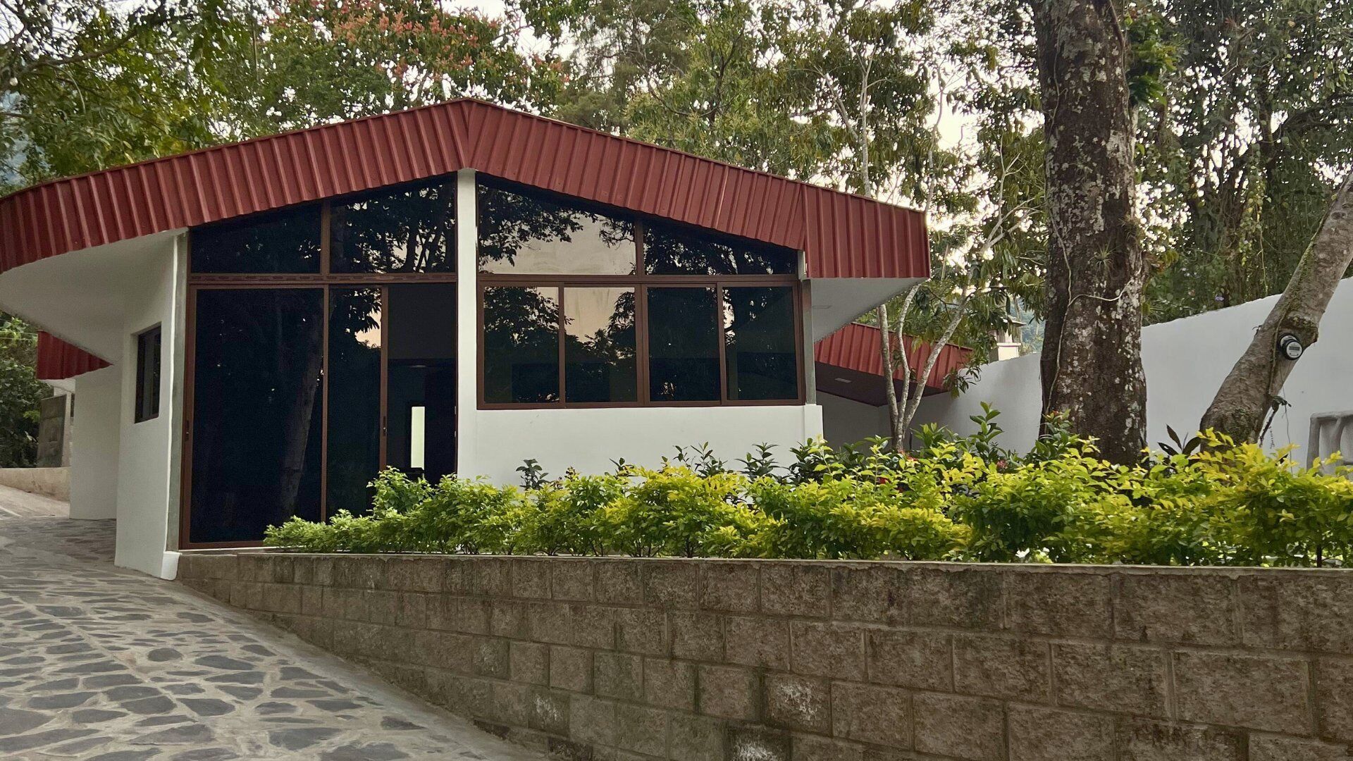 Un edificio moderno con tetto rosso e ampie finestre, immerso nel verde e circondato da un muro in pietra.