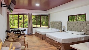 A hotel room with two beds, a dining table, chairs, and large windows offering a view of greenery. - Hotel Termales La Montaña (Ahuachapán)