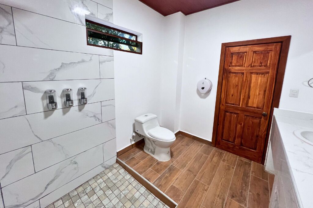 A bathroom with a toilet, a wooden door, and a shower area with a tiled floor.