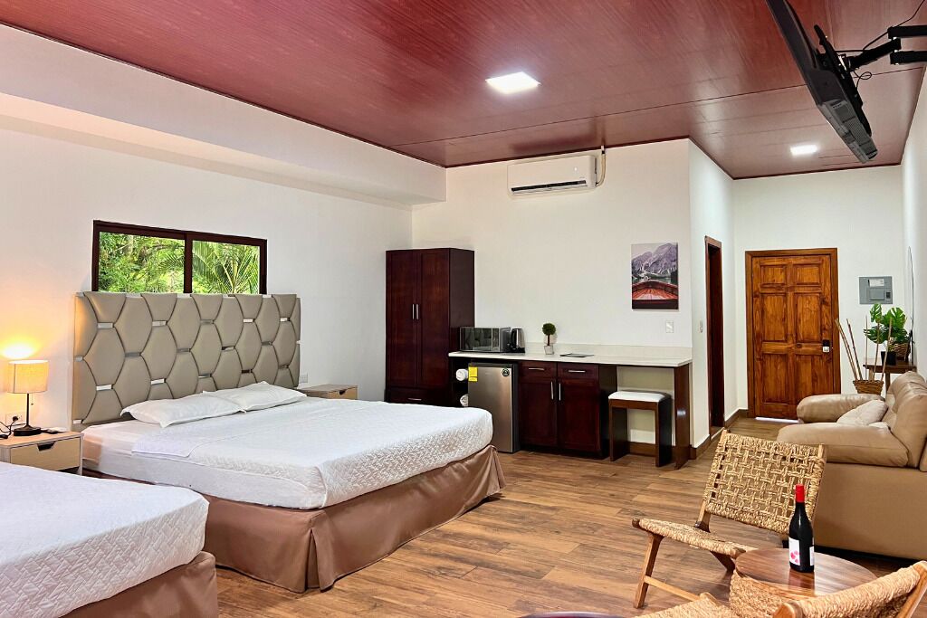 A hotel room with a large bed, a desk, a kitchenette, and a seating area with a chair and a sofa.