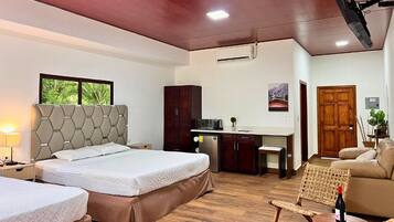 A hotel room with a large bed, a desk, a kitchenette, and a seating area with a chair and a sofa.