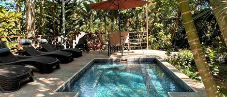 A rectangular pool with clear water, surrounded by lounge chairs and an umbrella.