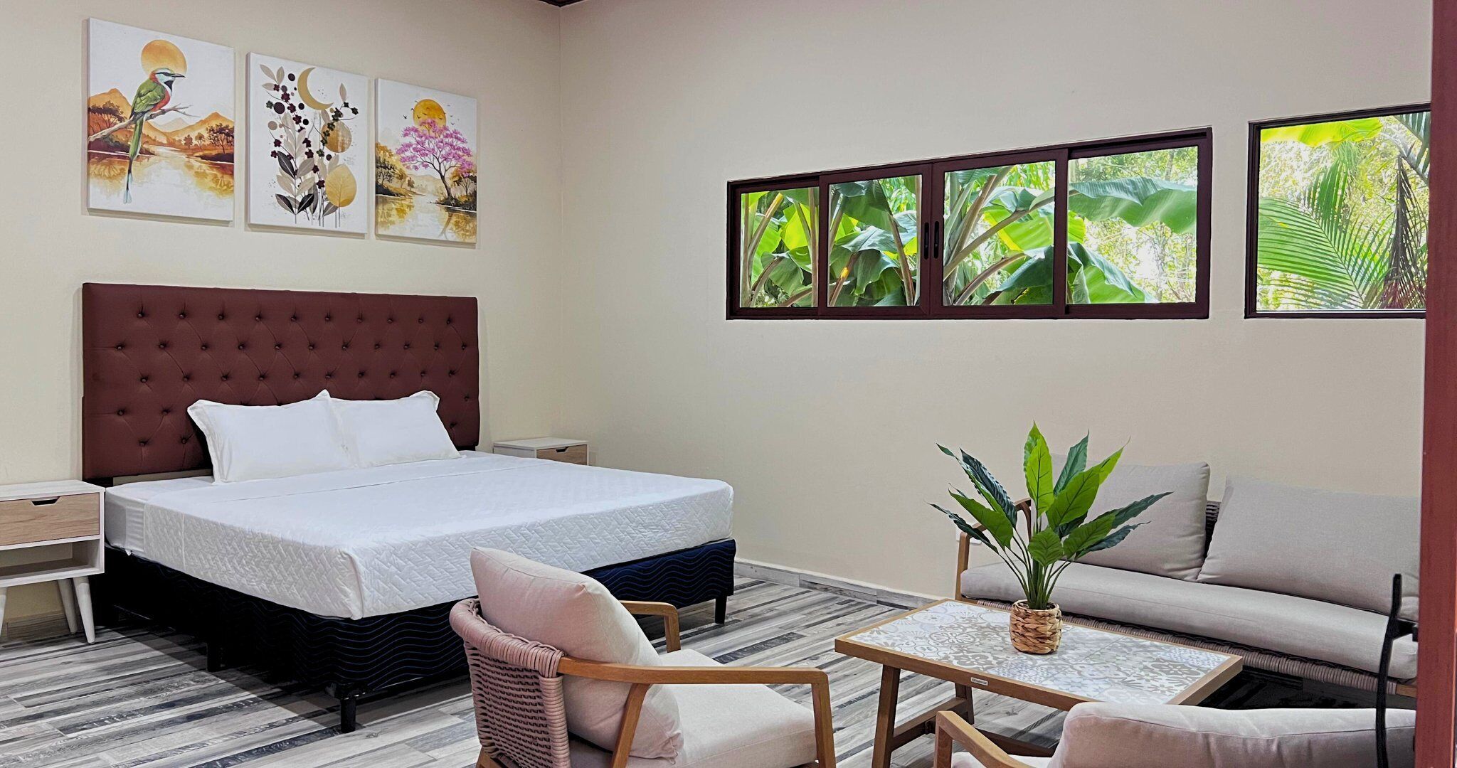 A hotel room with a large bed, a sofa, a small table, and a potted plant.