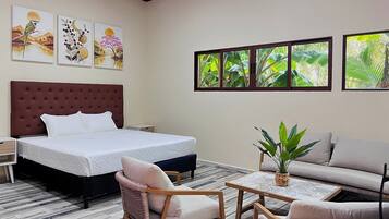 A hotel room with a large bed, a sofa, a small table, and a potted plant.