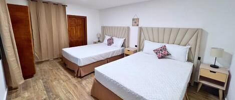 A hotel room with two beds, wooden flooring, and a wooden door.