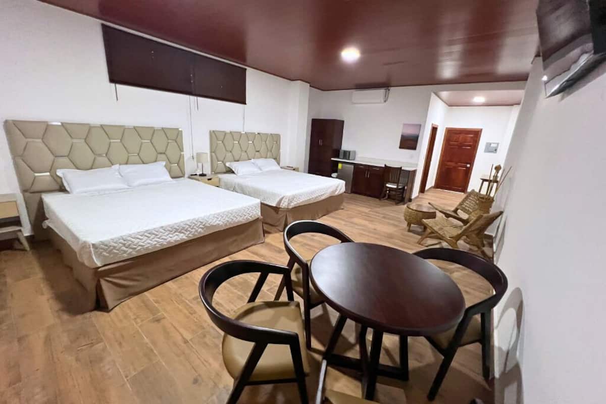 A hotel room with two beds, a dining table, and a small seating area.