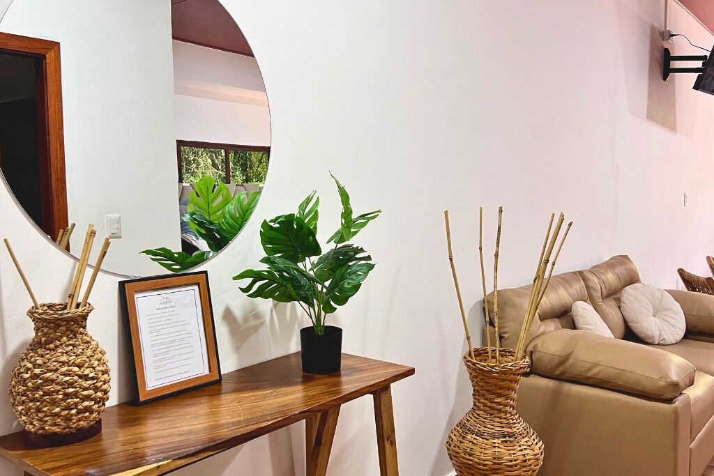 Una sala de estar con una mesa de madera, dos jarrones de mimbre, un certificado enmarco y una planta en maceta.